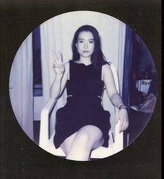 a woman sitting in a chair making the peace sign with her hand and wearing a black dress