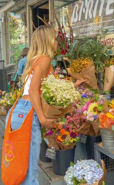 a woman standing in front of a flower shop with lots of colorful flowers on display