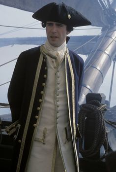 a man dressed in colonial clothing standing on the deck of a ship
