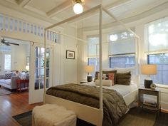 a bedroom with white walls and wood flooring has a four poster bed in the center