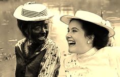 black and white photograph of two women in hats laughing at each other while they are covered in mud