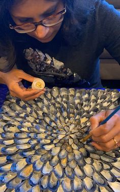 a woman is working on an art project with seashells in front of her