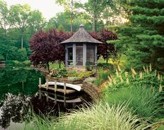 a gazebo in the middle of a pond surrounded by tall grass and trees with flowers around it