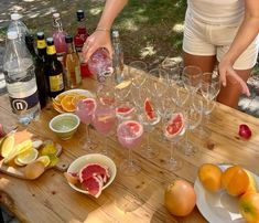 a woman pouring wine into glasses on top of a table filled with fruit and drinks