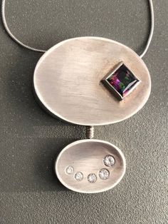 a silver pendant with two pieces of jewelry on it