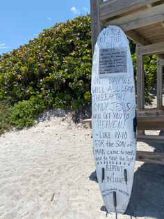 a white surfboard with writing on it sitting in the sand near a wooden structure