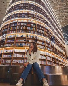 a woman sitting on the steps in front of a large book shelf filled with books