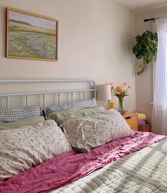 a bed with pink sheets and pillows in a bedroom next to a painting on the wall