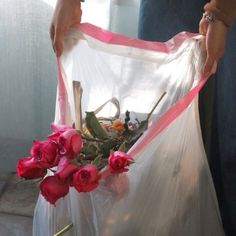 a person holding a plastic bag with flowers in it and pink ribbon around the bottom