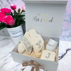 a gift box with two slippers and a mug in it, next to pink roses