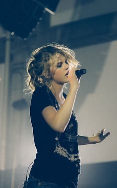 a woman standing on top of a stage holding a microphone in her hand and singing