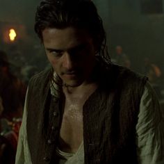 a man with long hair and no shirt standing in front of other men wearing vests