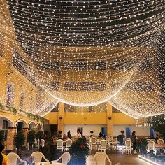 the inside of a building with tables and chairs covered in fairy lights on the ceiling