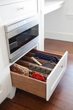 an open drawer with utensils and other items in it on a wooden floor