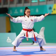 a woman standing on top of a blue mat in a karate ring holding her arms out