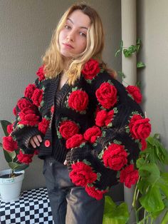 a woman standing next to a potted plant wearing a black and red sweater with roses on it