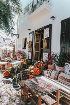 an outdoor seating area in front of a building with potted plants and fruit on the tables