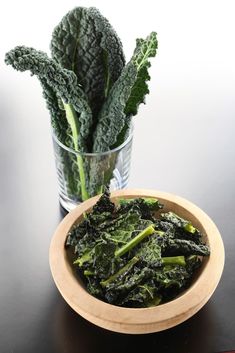 a wooden bowl filled with green vegetables next to a glass