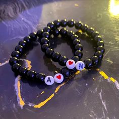 two beaded bracelets with hearts and letters on them sitting on top of a table