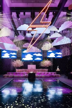 an empty dance floor is lit up with purple lights and clouds in the sky above it