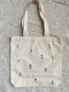 a white bag with embroidered flowers on it sitting on a bed next to a pillow