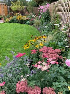 a garden filled with lots of flowers next to a lush green lawn and wooden fence