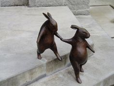 two bronze rabbits touching each other with their hands