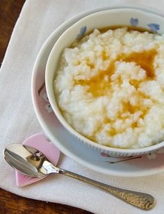 a white bowl filled with rice on top of a pink and white table cloth next to silverware