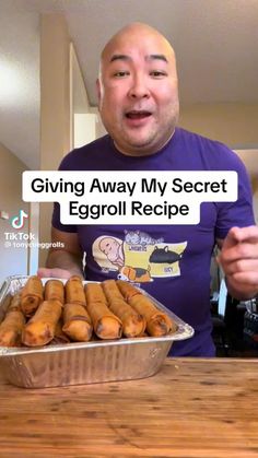 a man standing in front of a metal pan filled with eggrolls on top of a wooden table