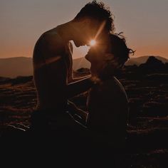 a man and woman kissing while the sun is setting in the sky behind them,