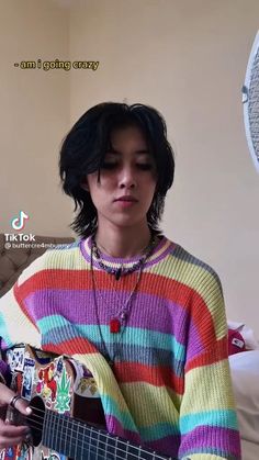 a person that is holding a guitar in their hand and wearing a colorful striped sweater