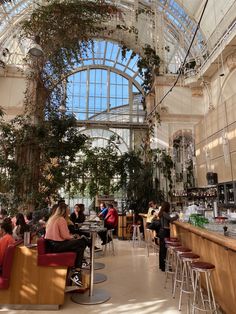 people are sitting at tables in the middle of a large room with high ceilings and tall windows