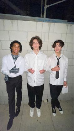 three young men standing next to each other in front of a white brick wall wearing ties