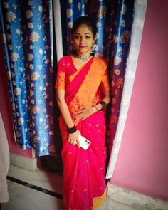 a woman in a pink and yellow sari standing next to a window with blue curtains