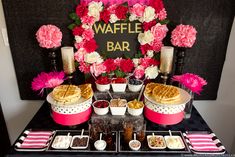 a waffle bar is set up on a table with pink flowers and desserts