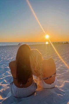 two women sitting in the sand watching the sun go down over the ocean and beach