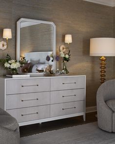 a white dresser sitting next to a chair in a living room under a large mirror