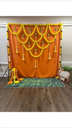an orange backdrop with yellow tassels and decorations on it, in front of a wooden floor
