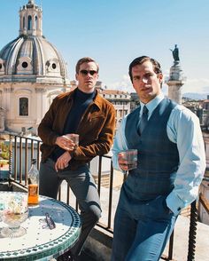 two men sitting at a table with drinks in front of the dome of a building