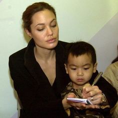 a woman is holding a child and looking at a cell phone while they are sitting down