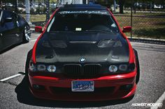 a red and black car parked in a parking lot next to another car with its hood up