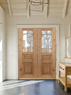 a large wooden door sitting inside of a white room next to a table and bench