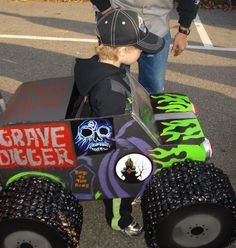 a young boy is standing next to a homemade grave digger car with skulls on it