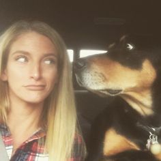 a woman sitting in the back seat of a car next to a large black and brown dog