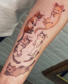 a woman's arm with cats on it and one cat sitting in the middle