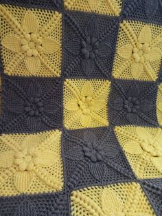 a crocheted blanket with yellow and gray squares on it, in the shape of flowers