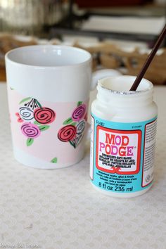 a white cup sitting on top of a table next to a jar of mod podge