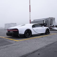 a white bugatti parked in a parking lot next to a semi - trailer