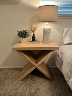 a small wooden table with a lamp on it next to a bed