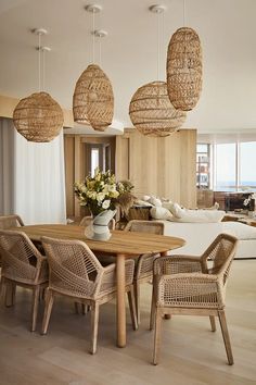 a dining room table and chairs with wicker hanging from the ceiling in front of an open living area